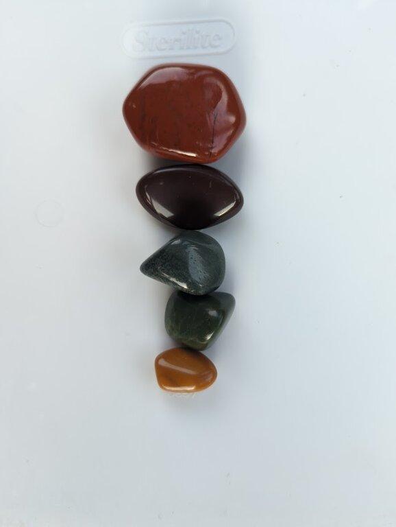 A closeup photo of several highly polished jaspers of various colors arranged on a white background.